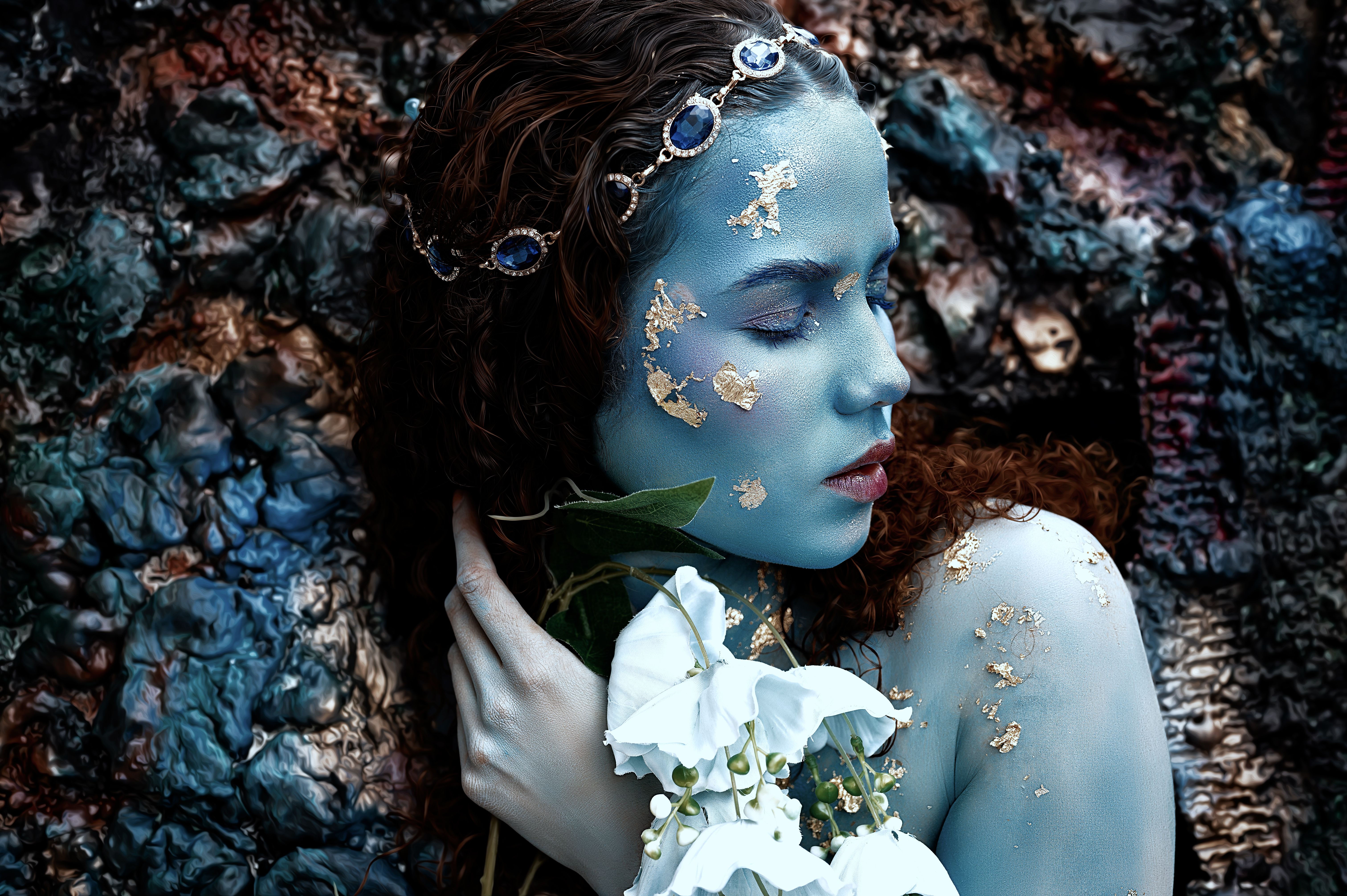 Artistic portrait of a woman with blue makeup and flower, evoking a dreamlike mood.