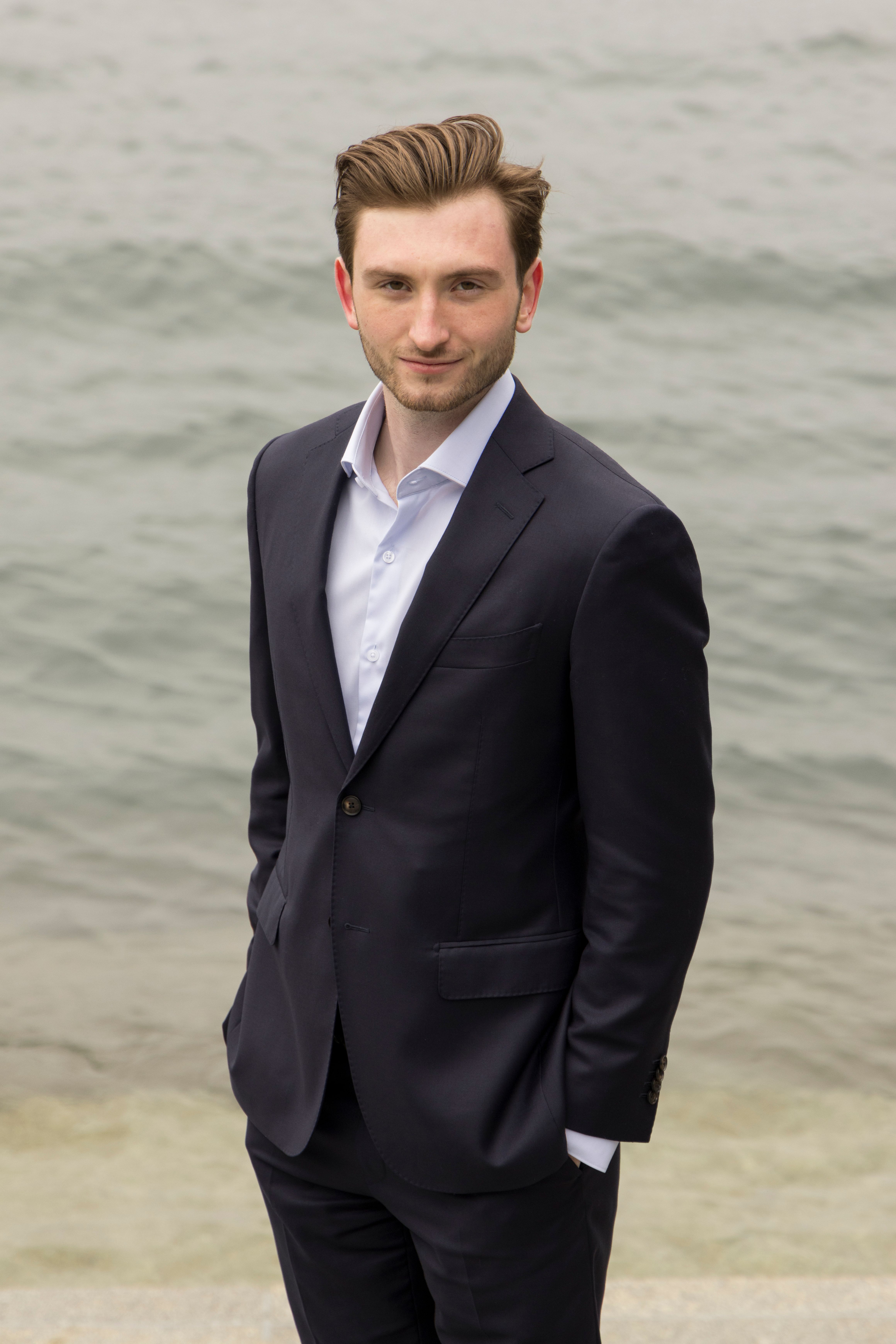 A confident businessman in a suit standing by the sea, exuding elegance and professionalism.