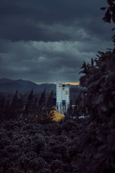 Industrial towers amidst a forest, with storm clouds creating a dramatic atmosphere.