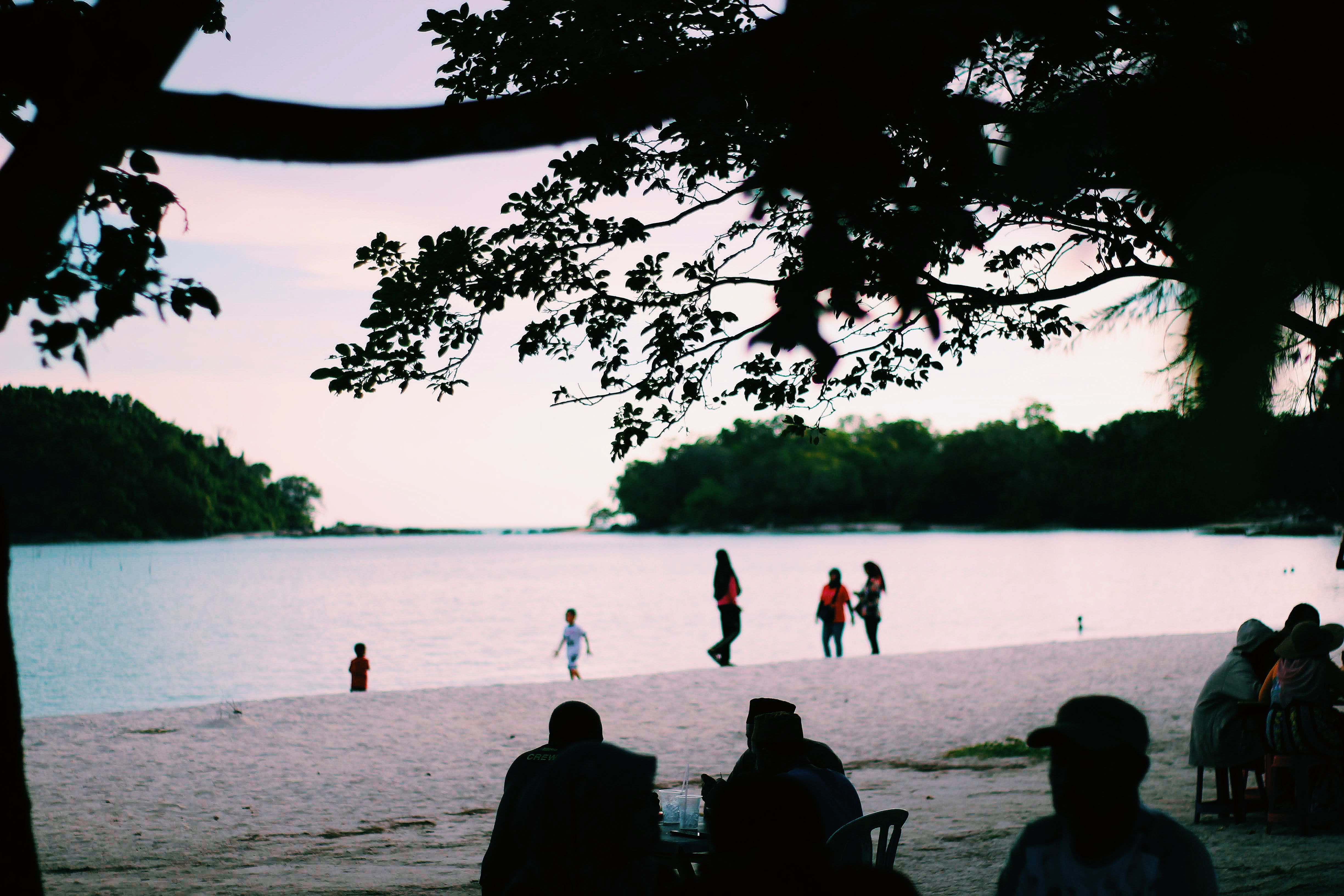 A beautiful beach scene in Kedah, Malaysia with people enjoying a colorful sunset.