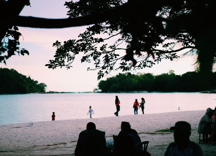 A beautiful beach scene in Kedah, Malaysia with people enjoying a colorful sunset.