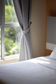 Sunlight illuminates a cozy bedroom interior with window view in Malaysia.