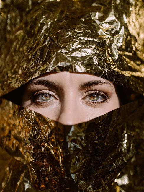 Elegant portrait of a woman partially concealed by gold foil, emphasizing her mysterious eyes.
