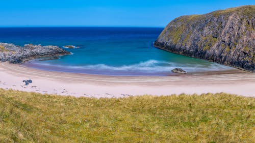 A beach with a grassy hill and blue water