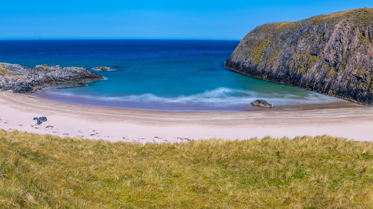 A beach with a grassy hill and blue water