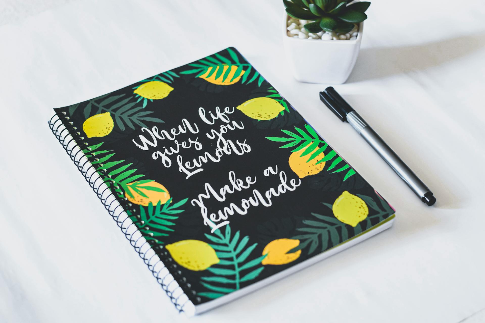 Spiral notebook with a motivational lemon-themed cover and a pen, perfect for journaling or note-taking.