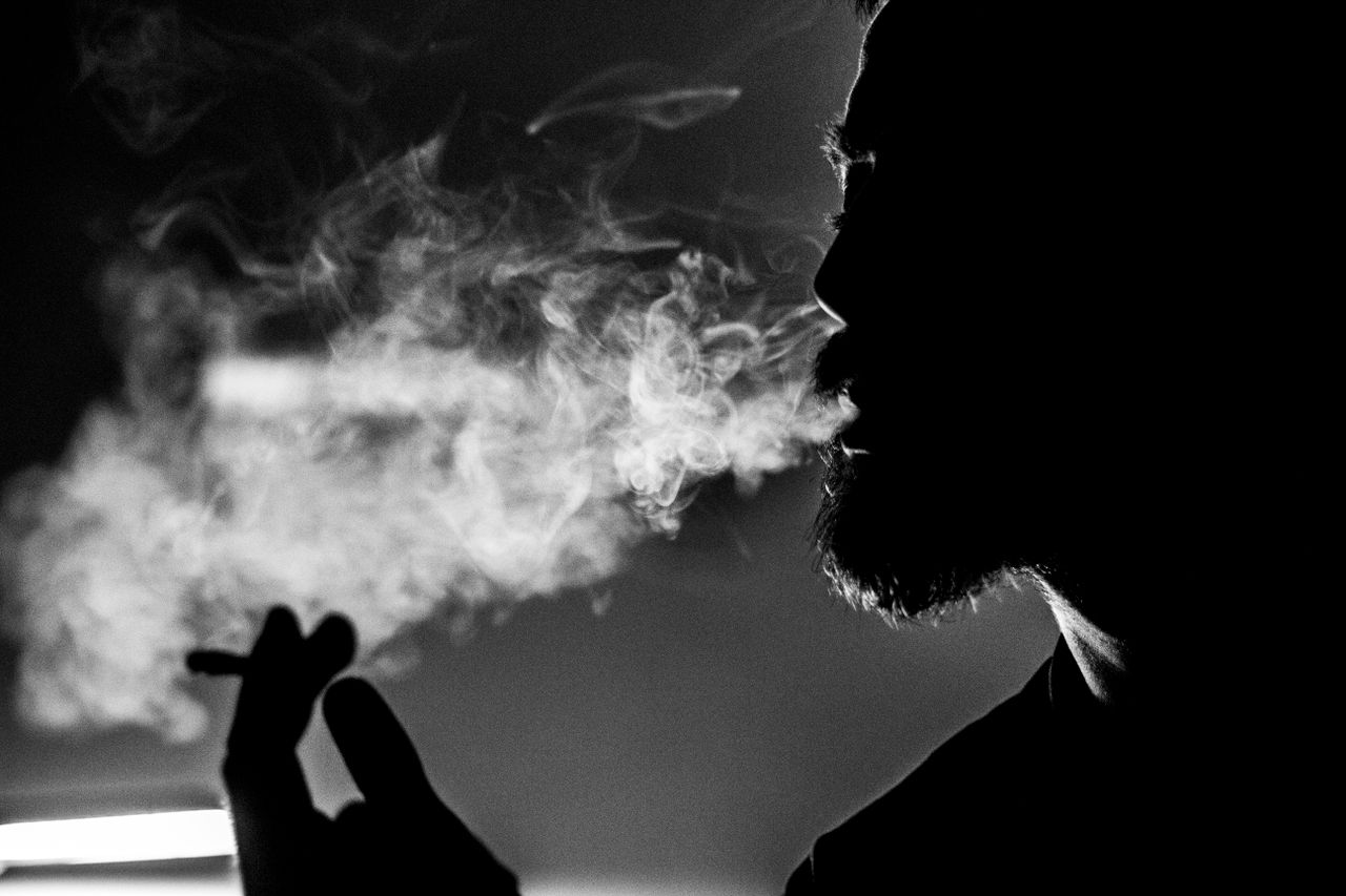 dramatic black and white photo of a man s silhouette exhaling smoke cr