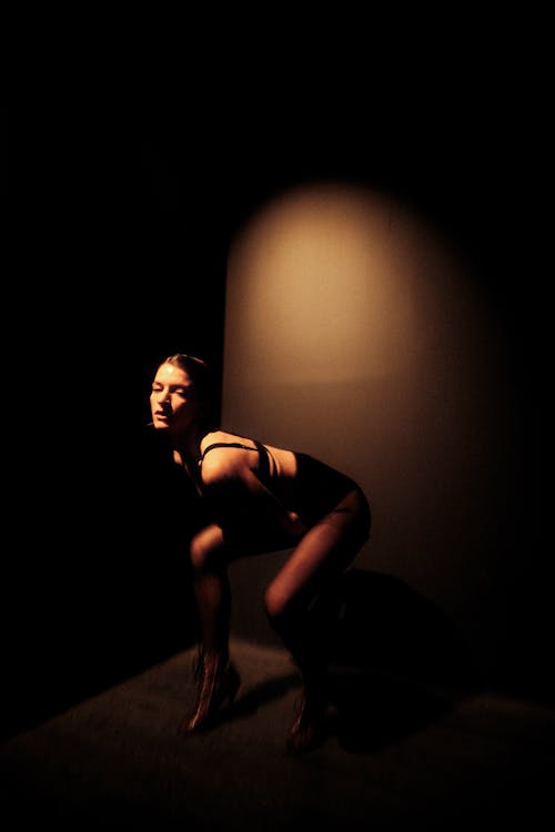 A woman in a black dress crouching in the dark