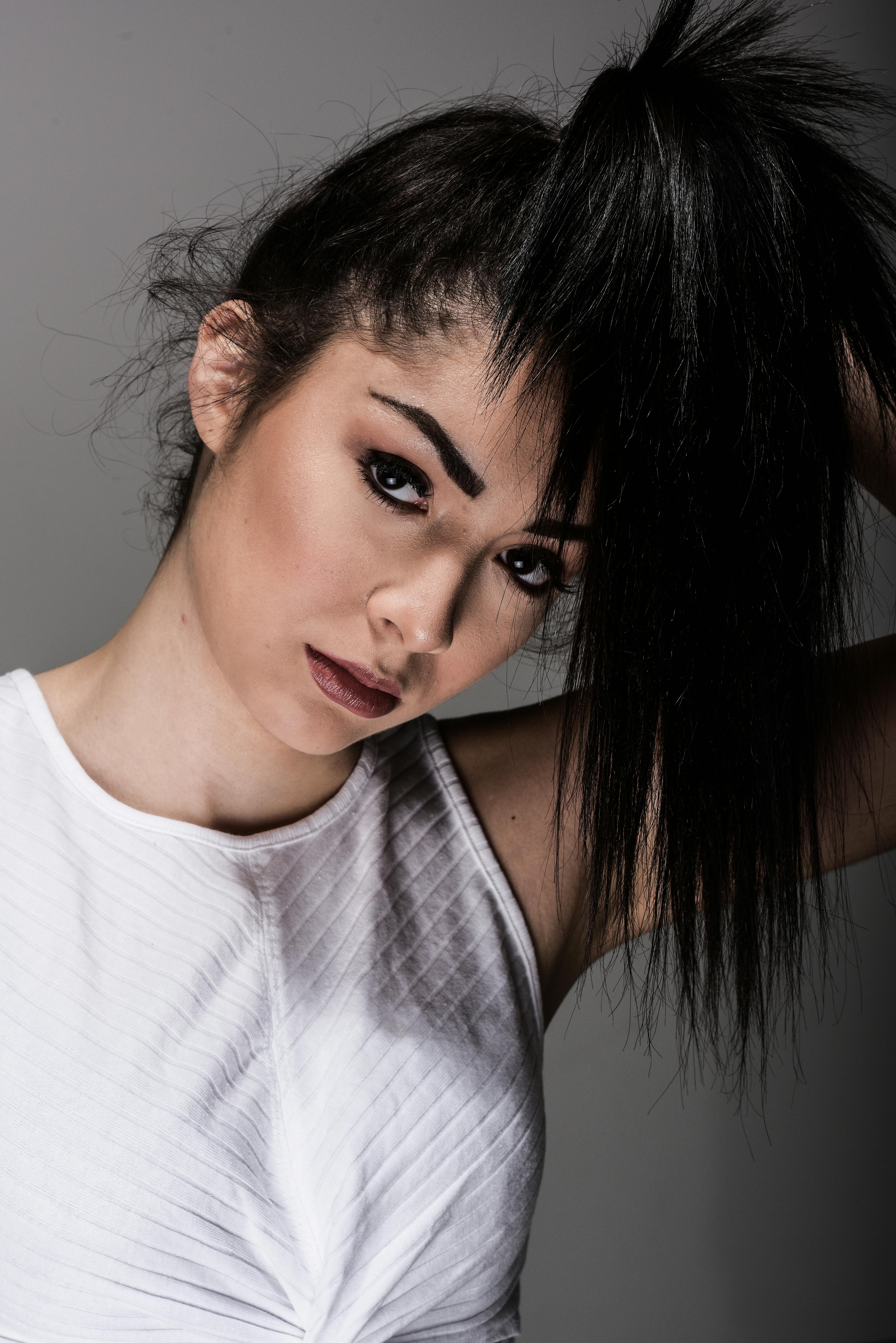 Portrait of a woman with black hair in white tank top, showcasing modern fashion in a studio setting.
