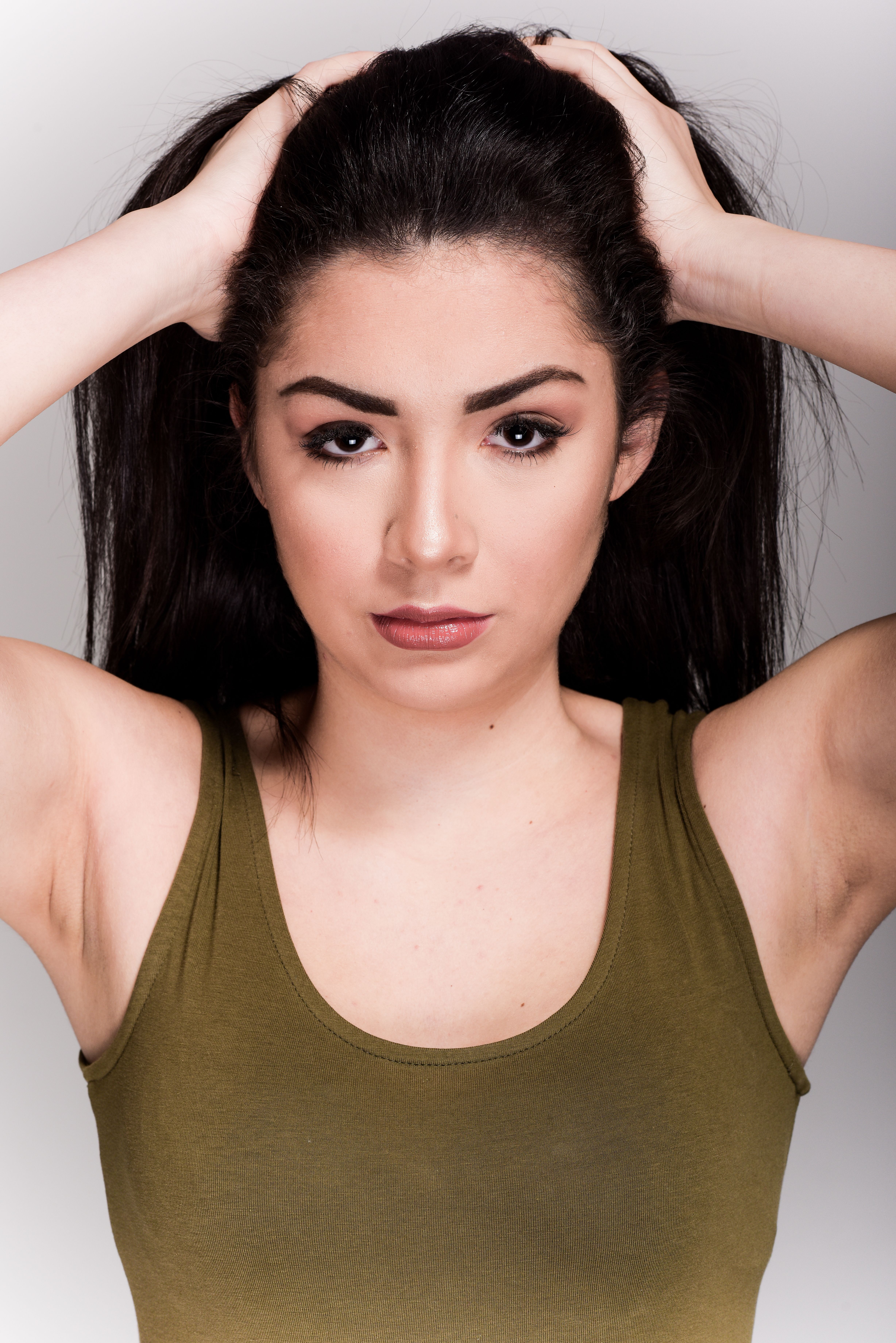 Portrait of a young woman posing confidently in a studio setting, hands in hair, wearing a tank top.