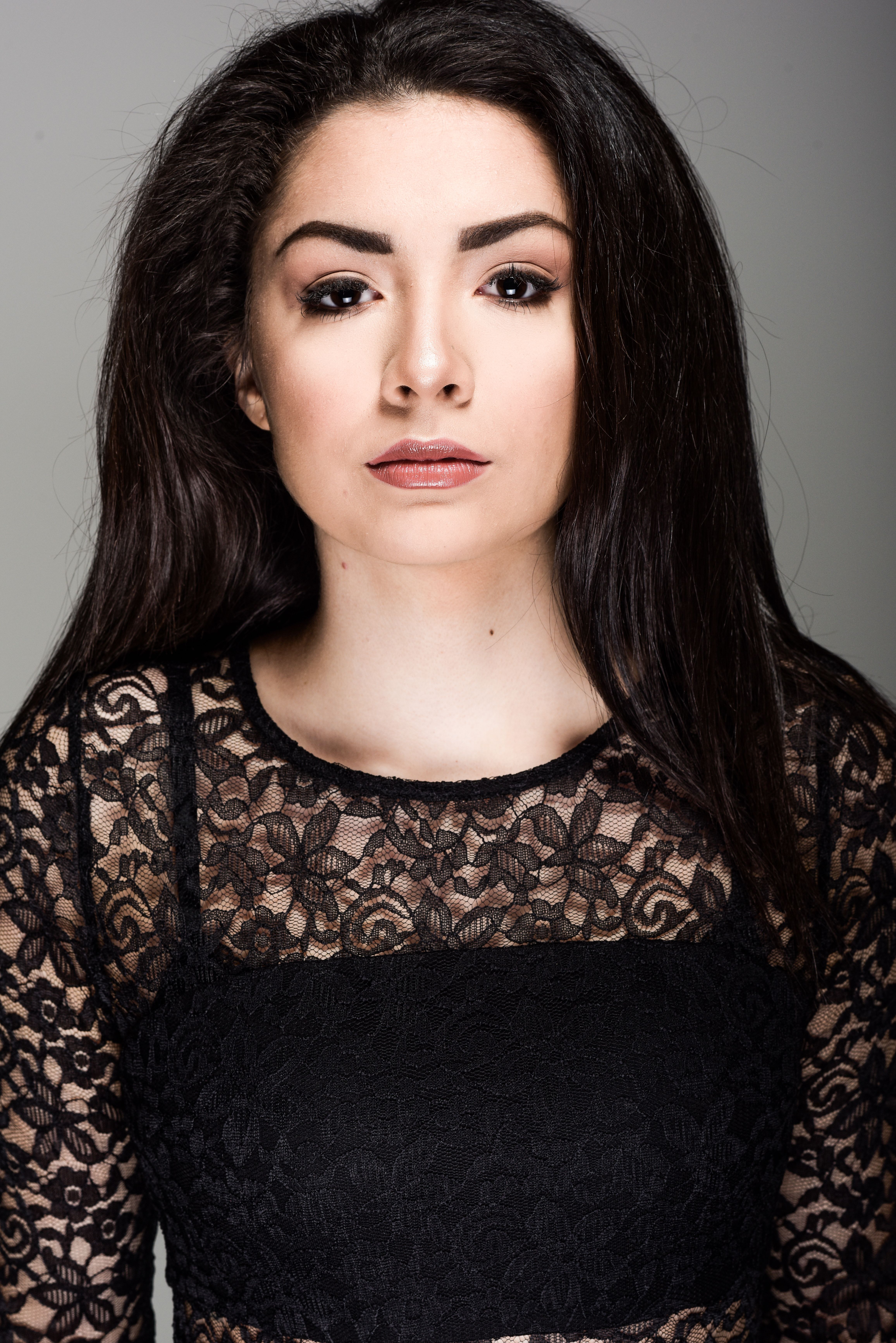 Portrait of a woman with long black hair wearing elegant lace in a studio setting.