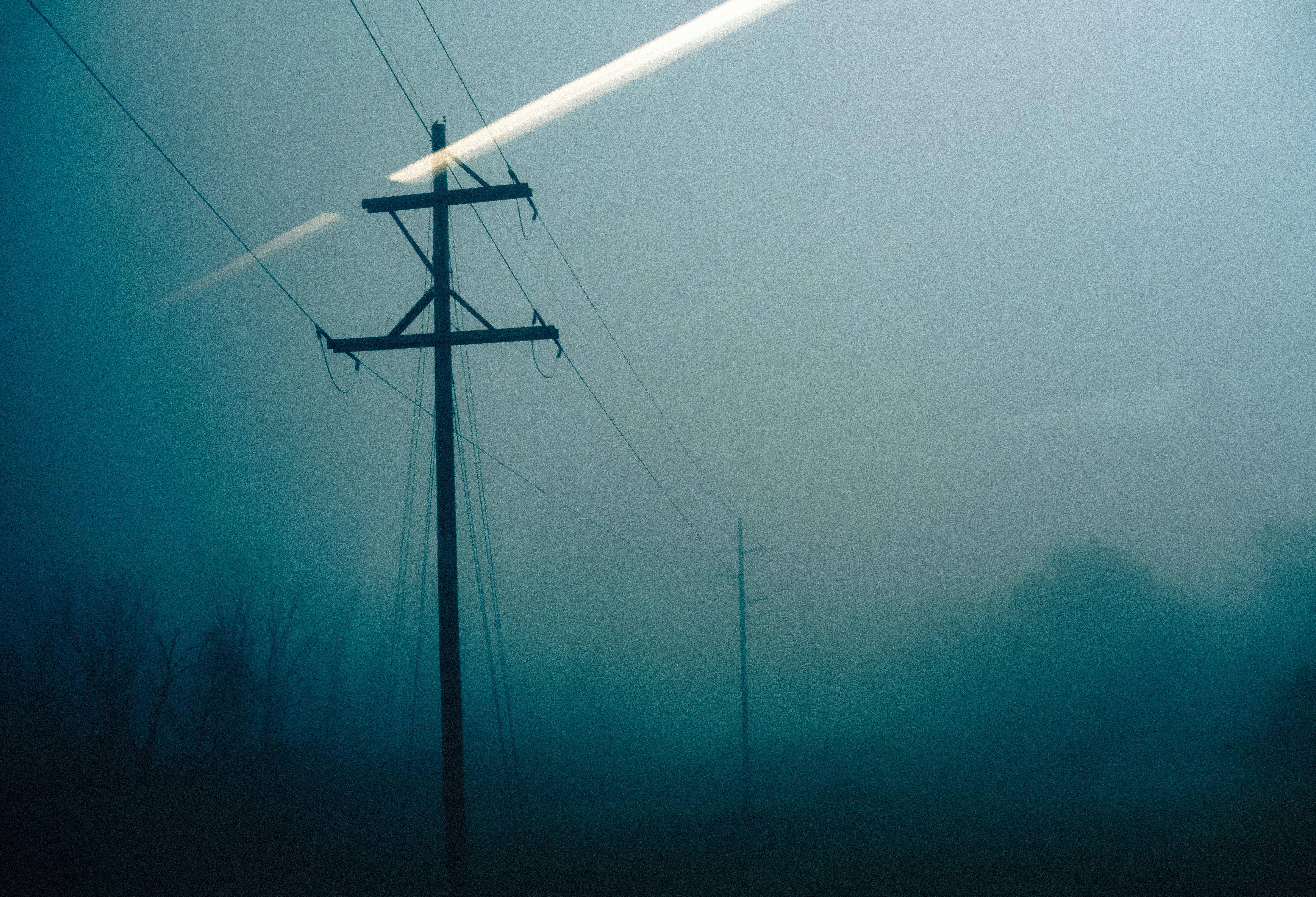 Silhouetted power lines in misty fog creating a mysterious landscape scene.