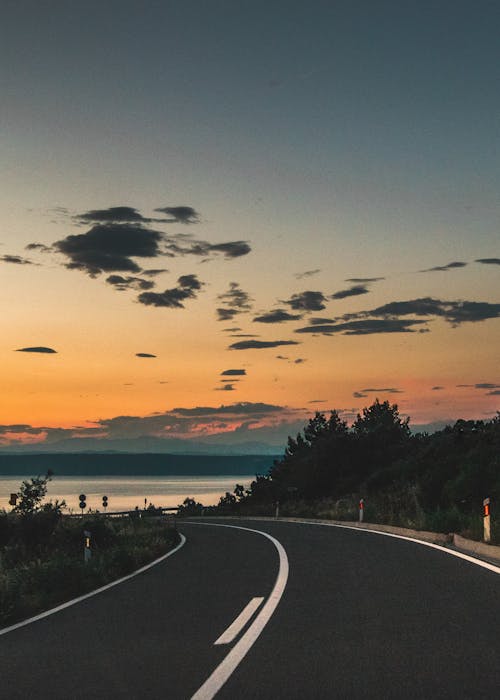 Gray Concrete Road Near Body of Water during Sunset