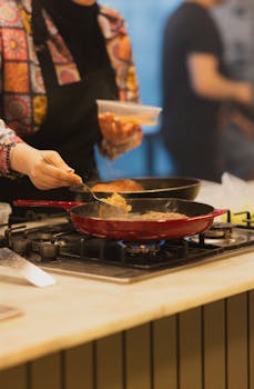 A chef preparing food on a stove with a focus on the cooking process in the kitchen.