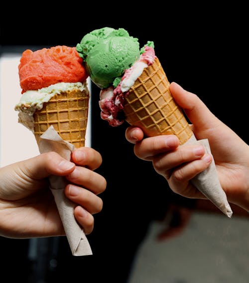 Two hands holding ice cream cones with colorful toppings