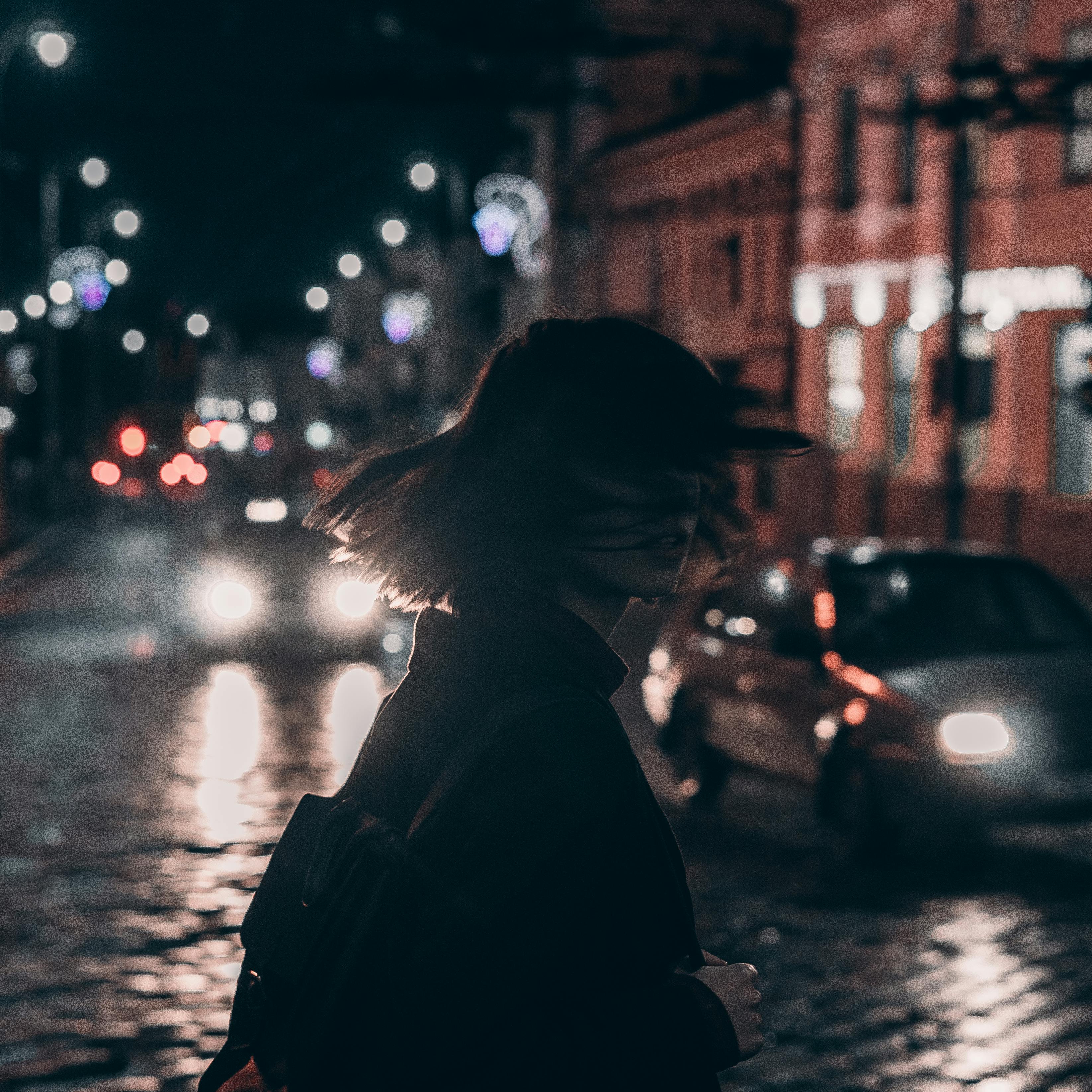 woman in black jacket carrying backpack with tousled hair walking on the street at night