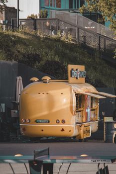 A vibrant yellow food truck serving doner kebabs in a lively urban park setting during summer.
