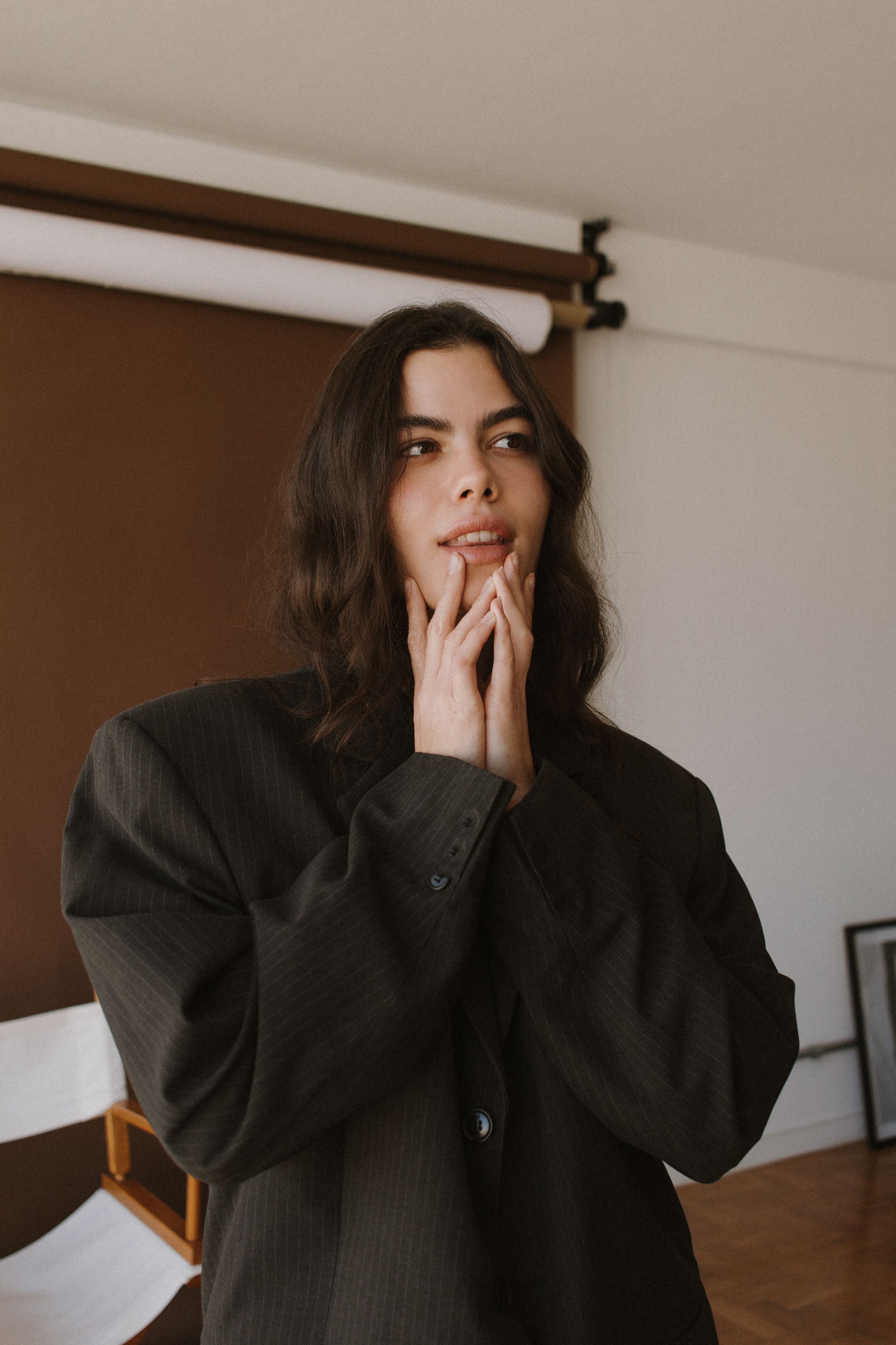 Portrait of a woman in stylish black outfit with hands on chin in a studio setting.