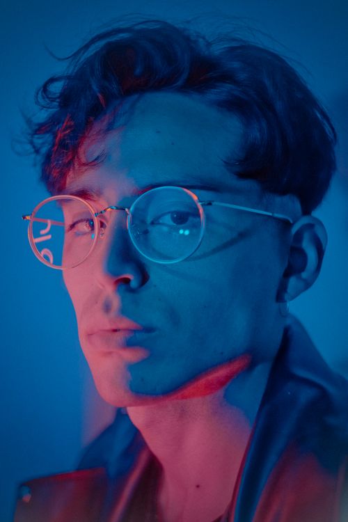 Free Artistic portrait of a man with eyeglasses, illuminated by vibrant pink and blue neon lights. Stock Photo