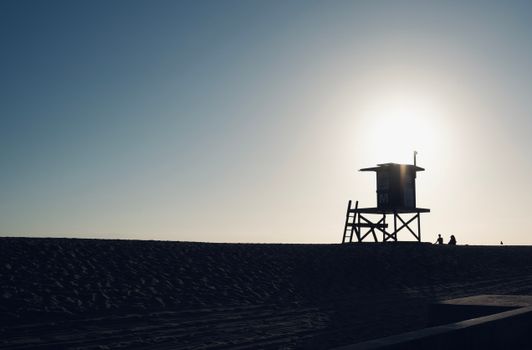 Silhouette of a lifeguard tower on a sandy beach during sunset, creating a calm and serene atmosphere.