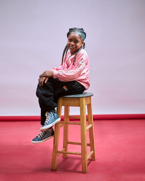 A young girl sitting on a stool in front of a red background