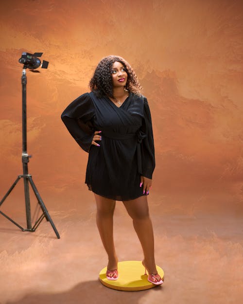 A woman in a black dress standing on a yellow background