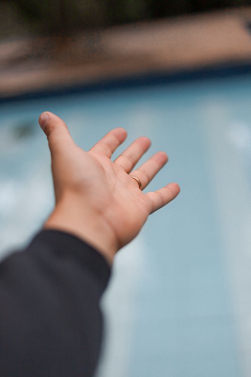 Free Close-up of an outstretched hand with a wedding ring over a blurred pool background. Stock Photo