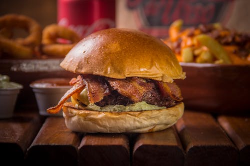 A burger with bacon and onion rings on a wooden table