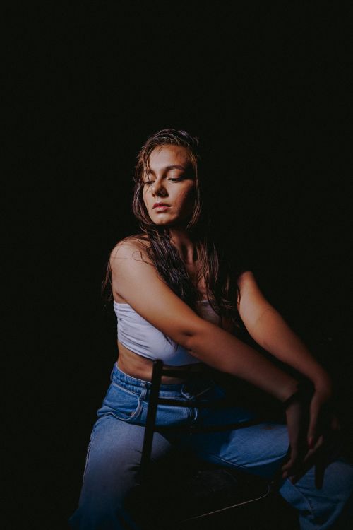 Free Artistic portrait of a woman in a studio, illuminated by a spotlight, wearing a white crop top and jeans. Stock Photo