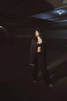 A fashionable woman poses confidently in a dimly-lit industrial warehouse, creating a moody atmosphere.