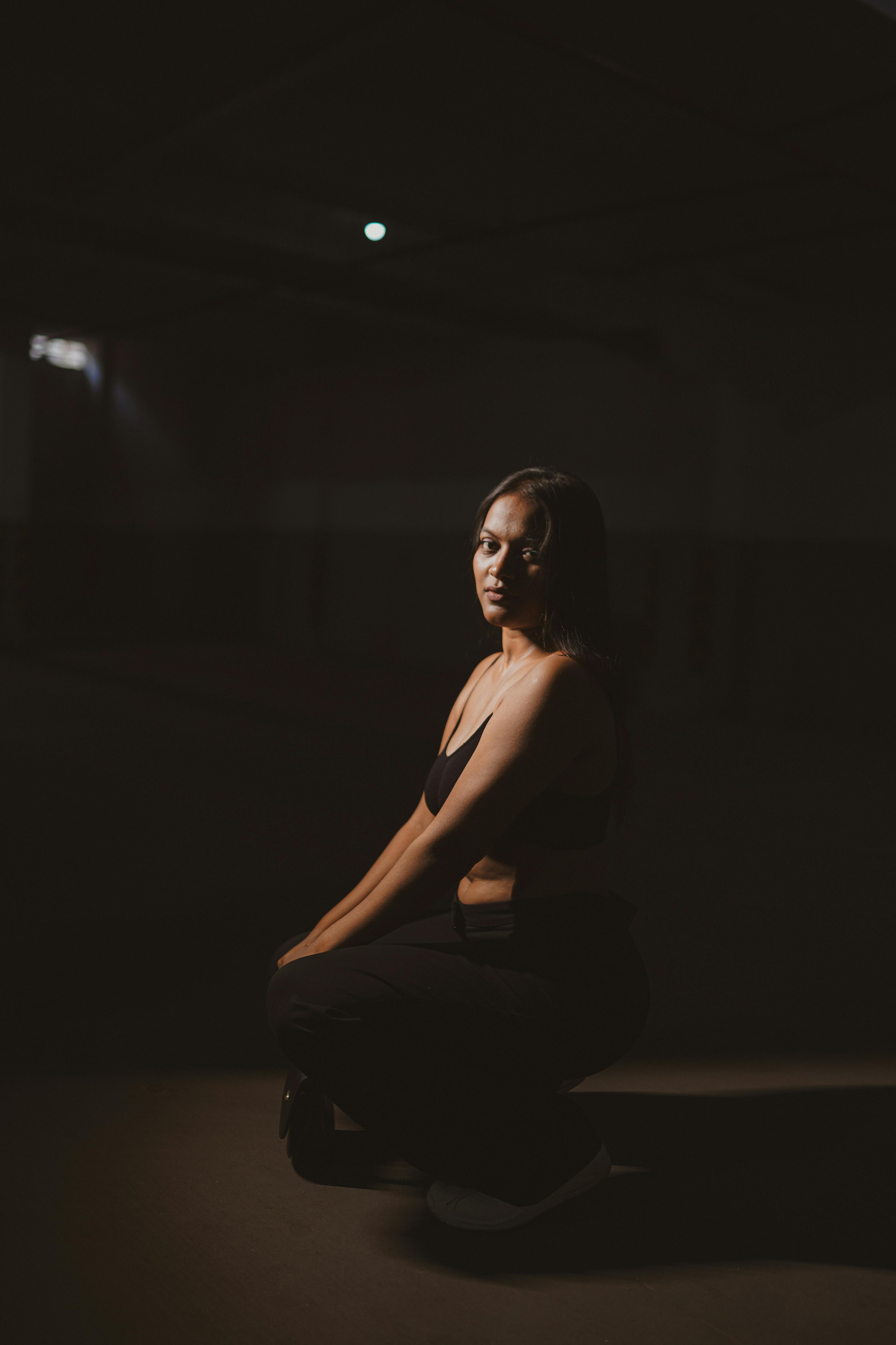 Artistic portrait of a woman kneeling in shadowy lighting, exuding mystery.