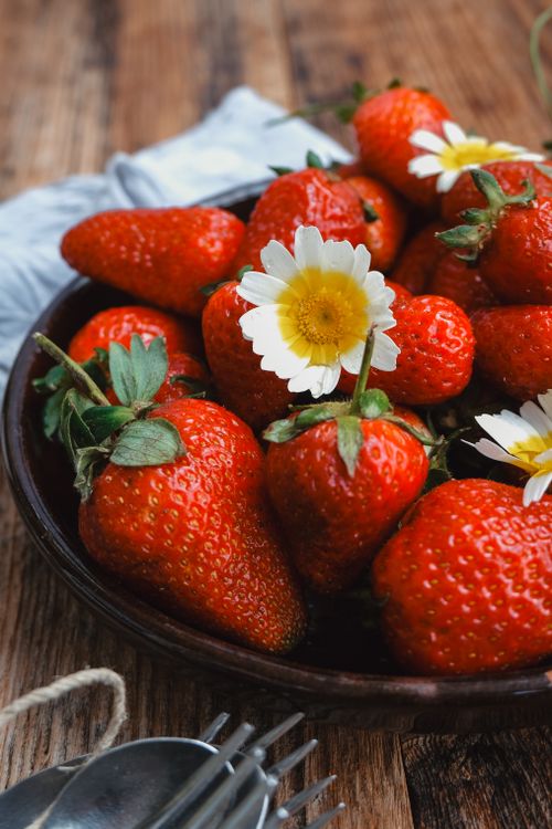 Free A rustic bowl filled with ripe strawberries and daisies on a wooden table, evoking summer freshness. Stock Photo