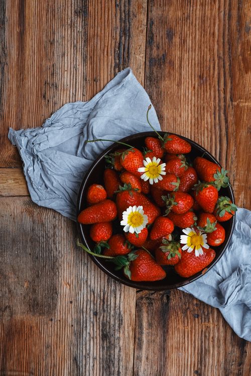 Free Top view of a bowl of ripe strawberries with daisies on a rustic wooden table, creating a fresh and natural scene. Stock Photo