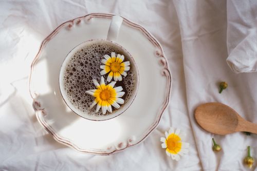 Free A rustic cup of herbal tea with daisies on a white bedspread for a cozy morning vibe. Stock Photo