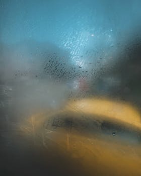 Steamy and blurred view through a rainy window featuring a distinct yellow glow and city backdrop.