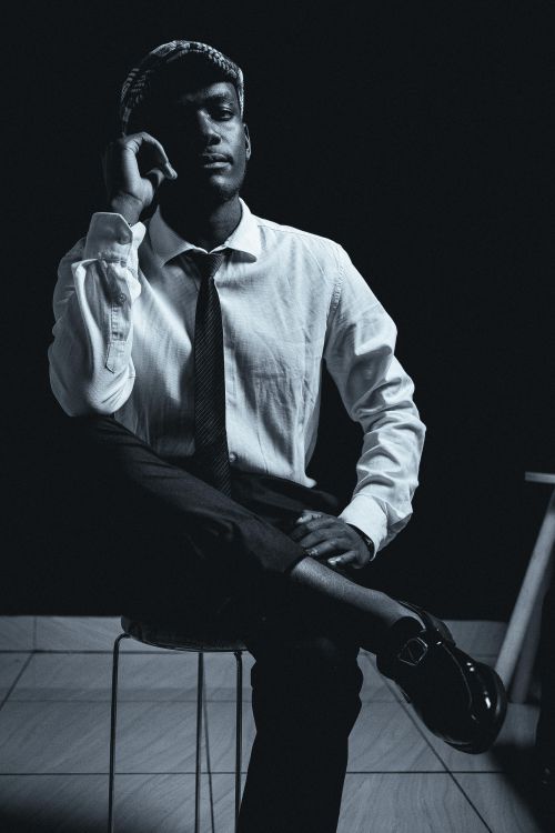 Free Elegant black and white portrait of a thoughtful man in stylish attire seated in a studio. Stock Photo