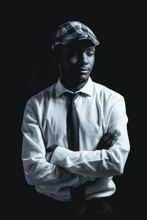 Free Portrait of an African American man in a flat cap and tie, styled in black and white, exuding timeless fashion. Stock Photo
