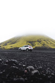 Silver SUV on a black volcanic dirt road with lush green mountain backdrop in Iceland.