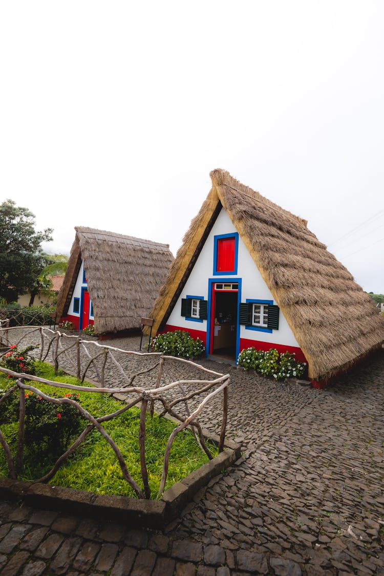 Traditional Red, Blue And White Houses With Thatched Roofs In Santana, Madeira Island, Portugal