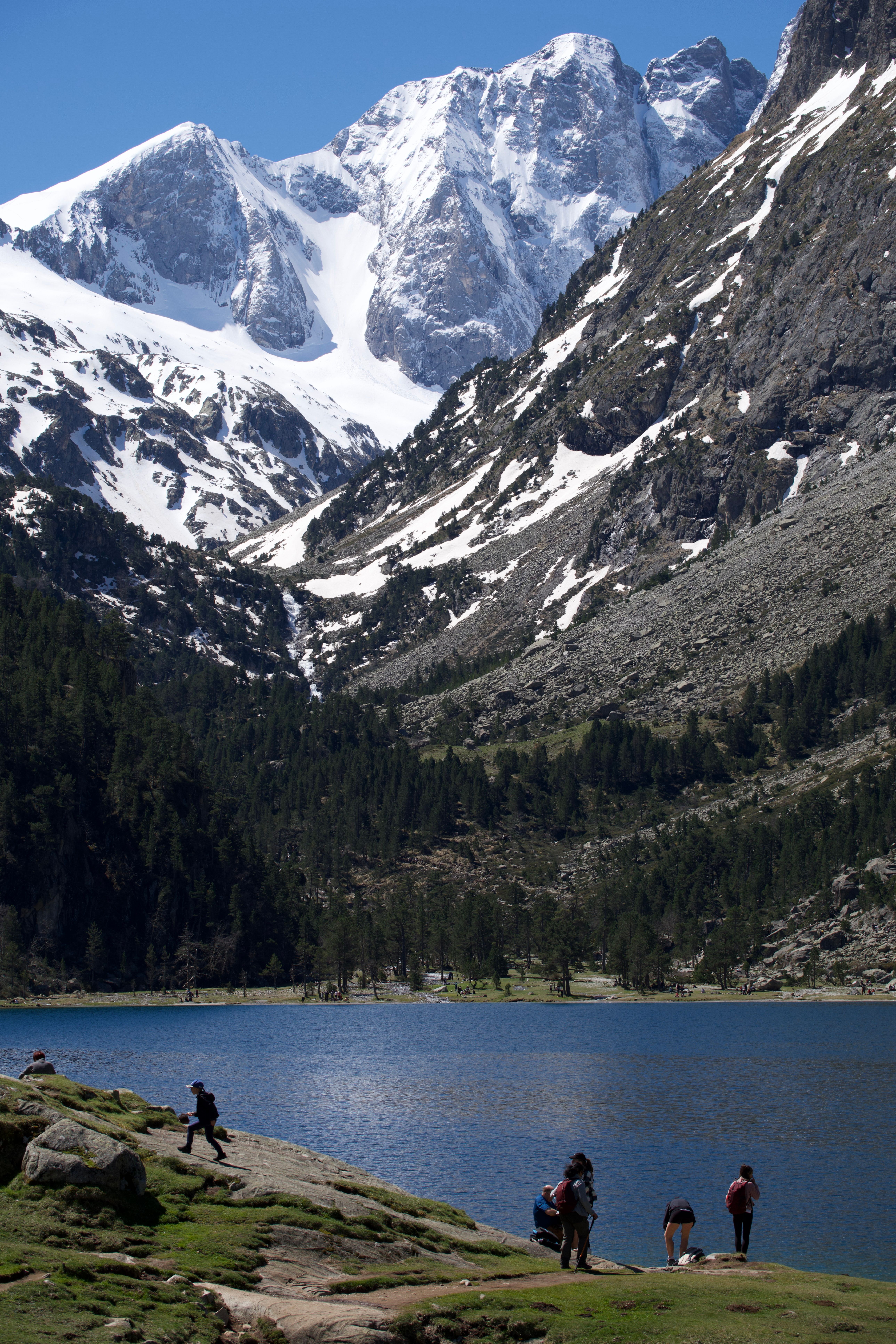 People exploring a picturesque mountain lake surrounded by snow-capped peaks in summer.