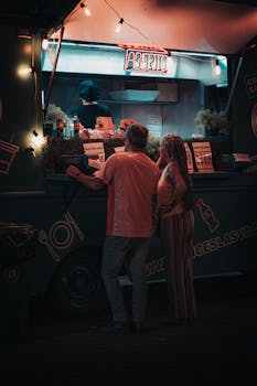 A couple orders food at a vibrant street food truck at night, showcasing the bustling gastronomy scene.