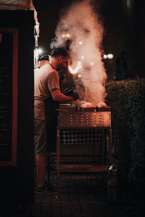 Free A man grilling food at night with smoke rising creates a warm atmosphere. Stock Photo
