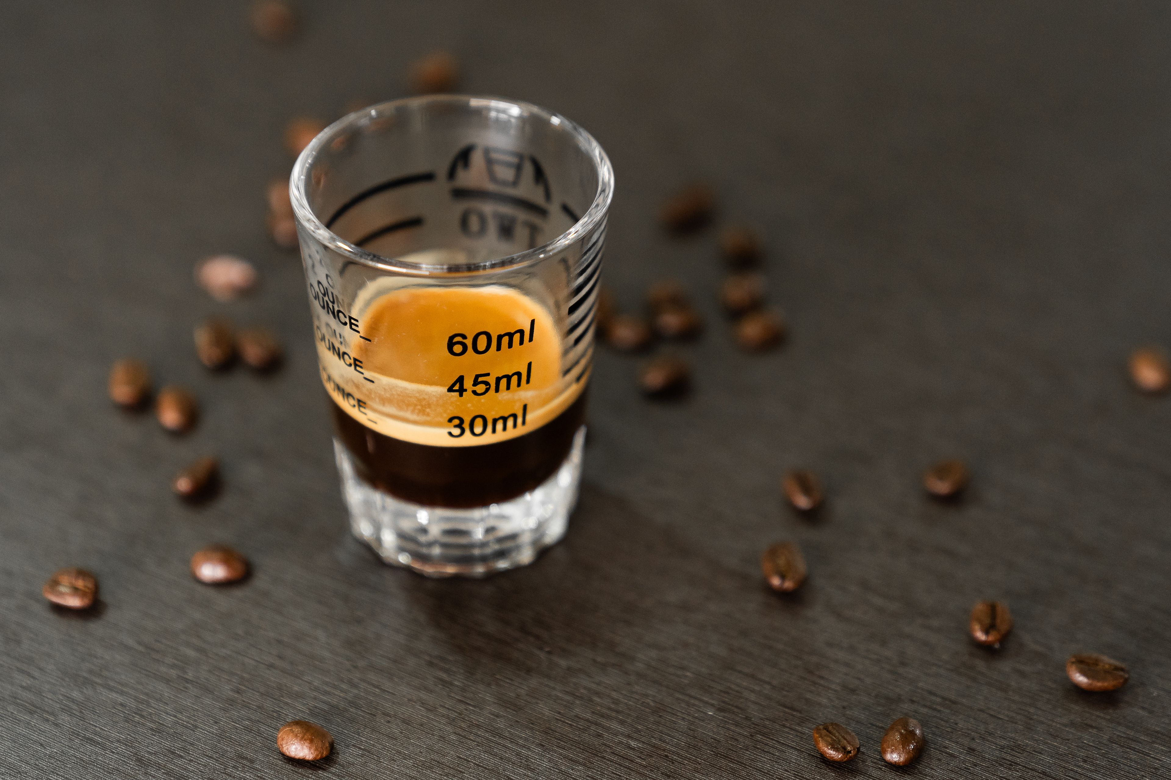 Shot espresso dans un verre doseur entouré de grains de café, vue minimaliste