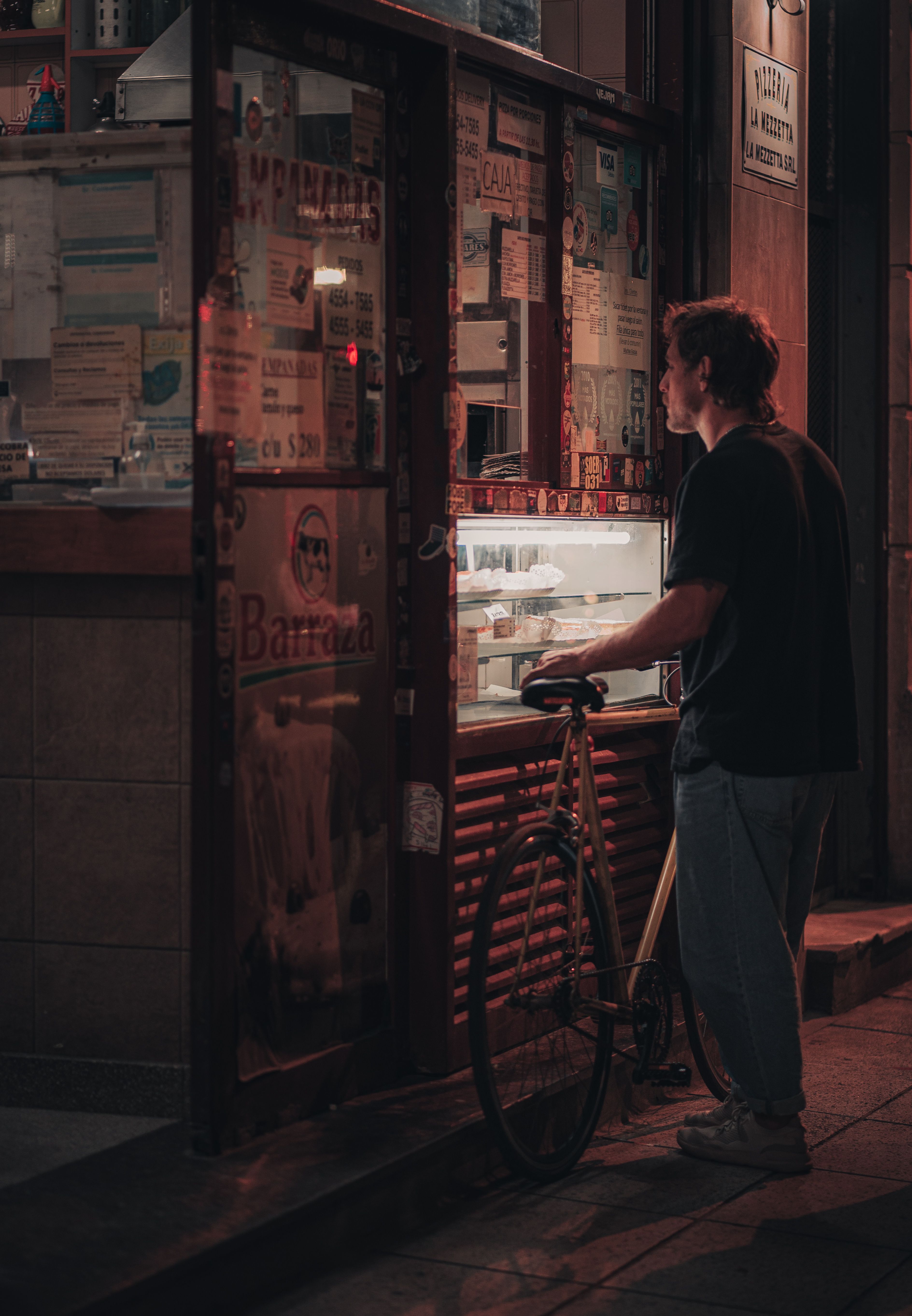 A man with a bicycle at a street food vendor during night in the city. Urban ambiance captured creatively.