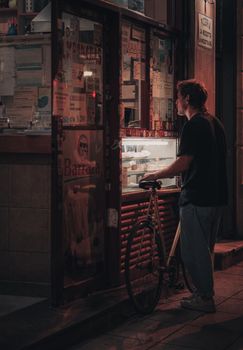 A man with a bicycle at a street food vendor during night in the city. Urban ambiance captured creatively.