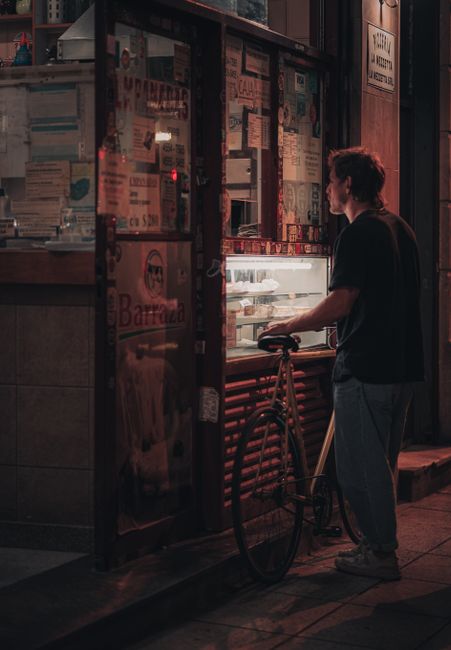 A man with a bicycle at a street food vendor during night in the city. Urban ambiance captured creatively.