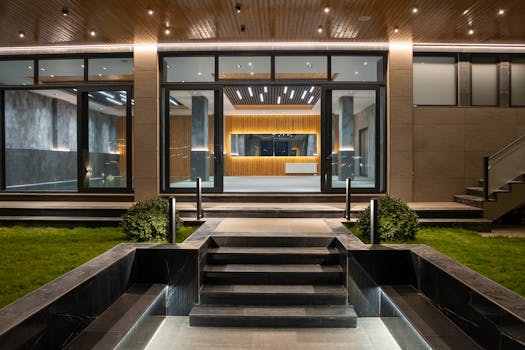 Elegant illuminated entrance to a modern luxury house at night with landscaped garden.