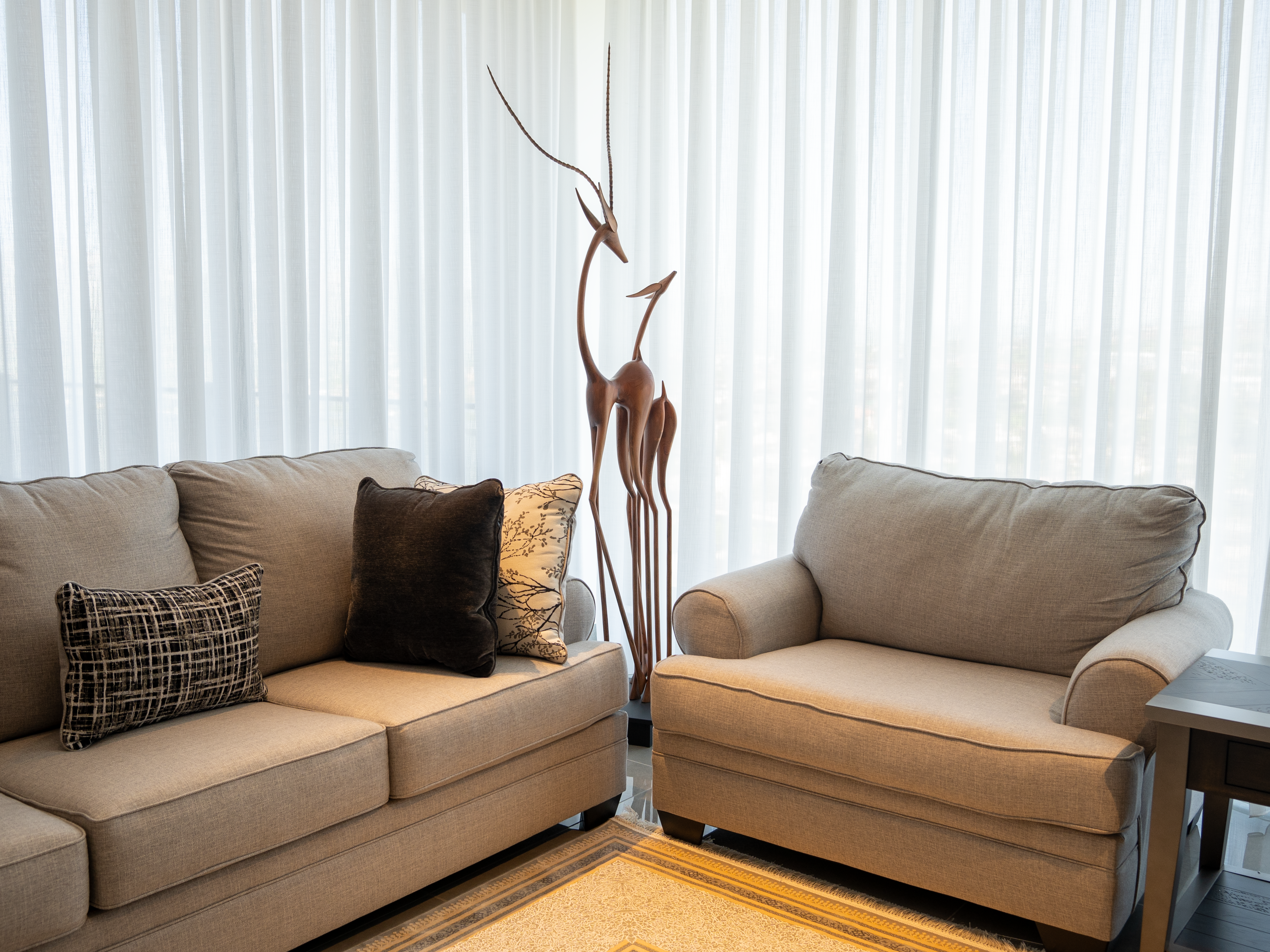 An elegant living room with beige sofas, artistic deer sculpture, and sheer curtains.