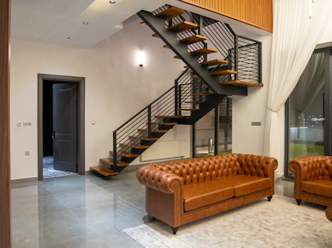 Stylish interior design featuring leather sofas, staircase, and open space.