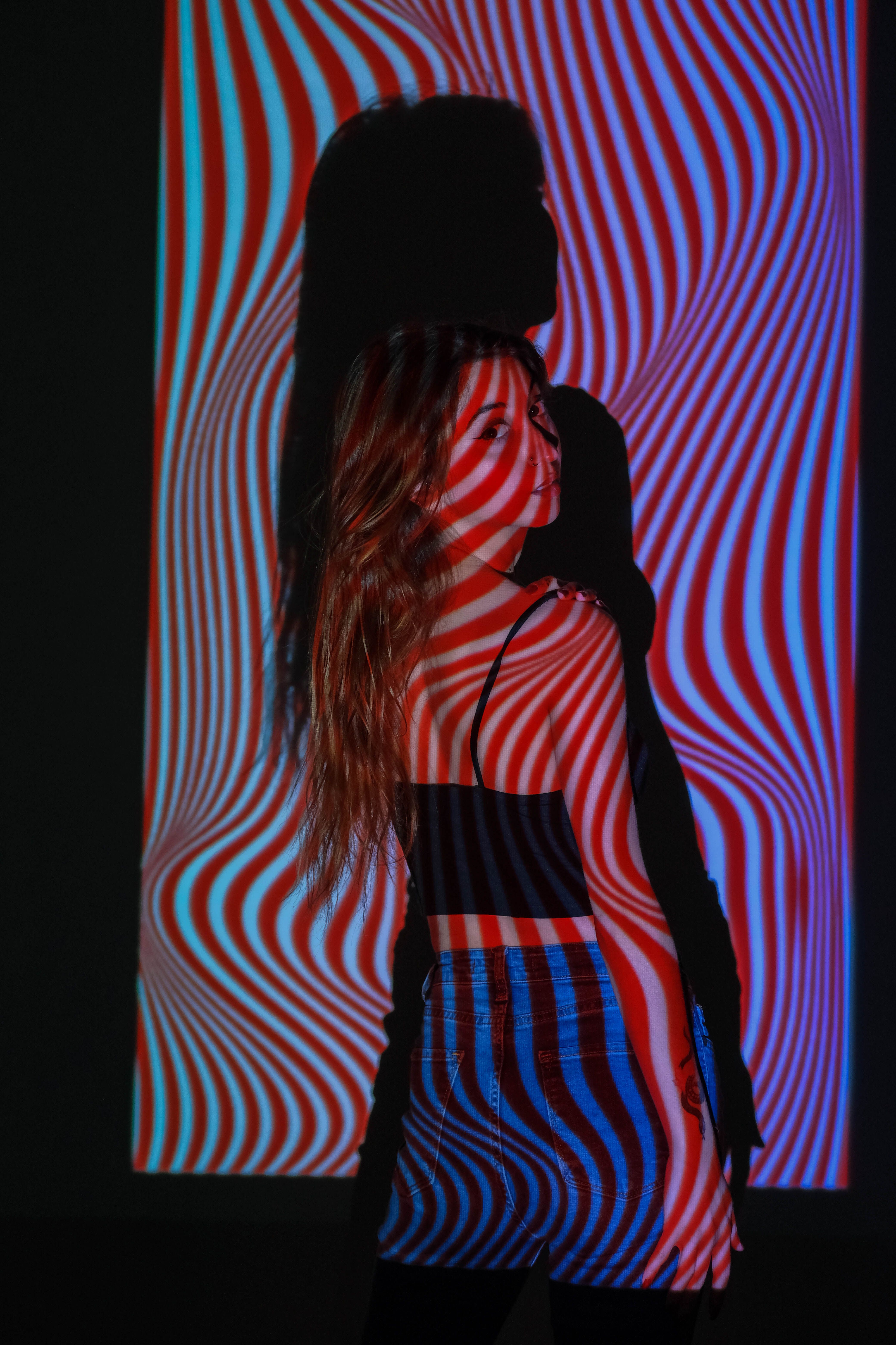 Artistic portrait of a woman with vivid red and blue striped light patterns projected onto her indoors.
